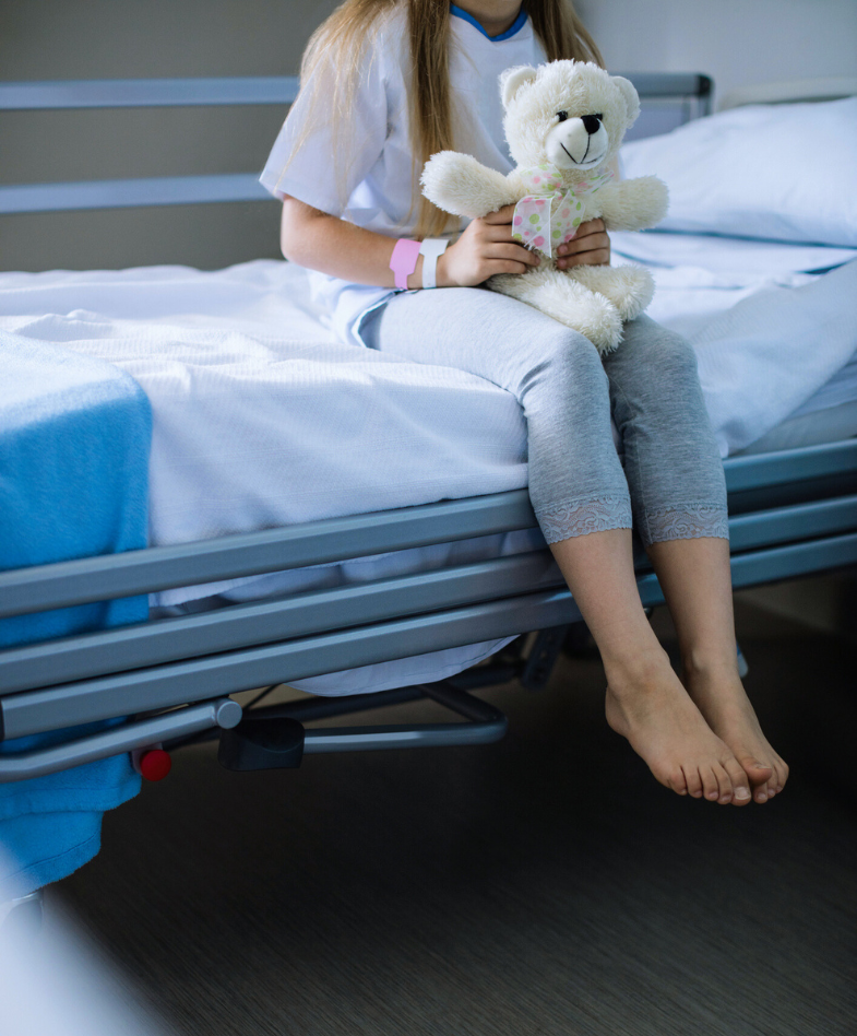 Child holding teddy sitting on hospital bed