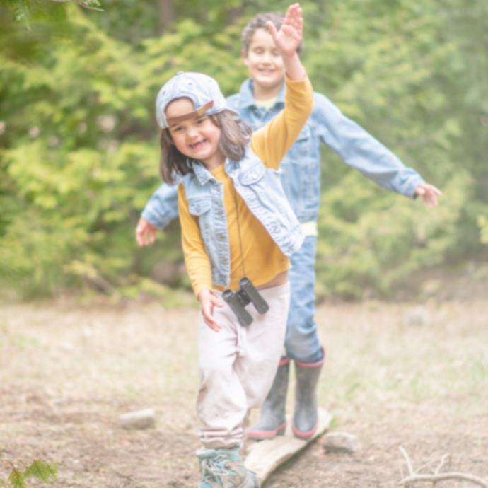 two smiling young children walking along a log 