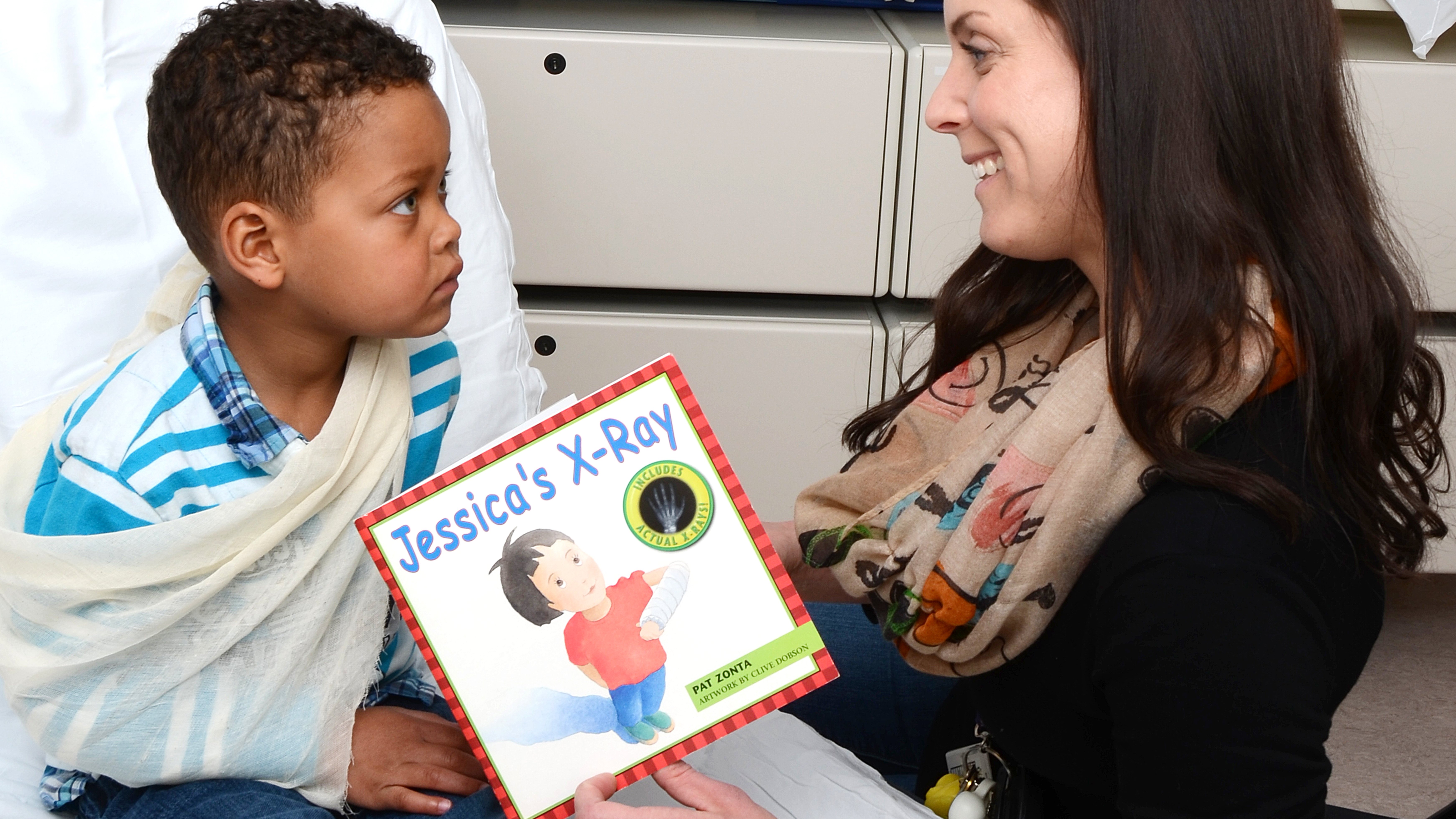 Woman reading book to small boy with sling