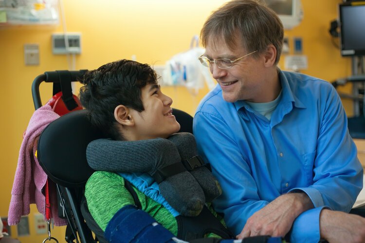 Smiling youth in wheelchair talking to adult 