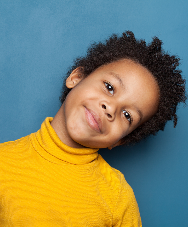 A young boy with a yellow turtle neck on standing in front of a blue background
