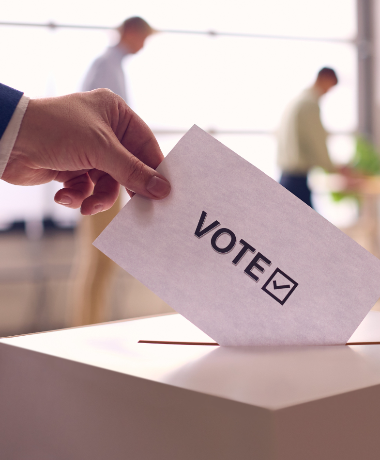 A hand dropping a voting card into a voting box.