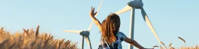 Young girl running through a field of wheat with wind mills 