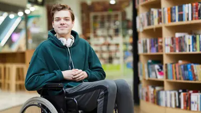 a teenage boy in a wheelchair sitting in a library smiling
